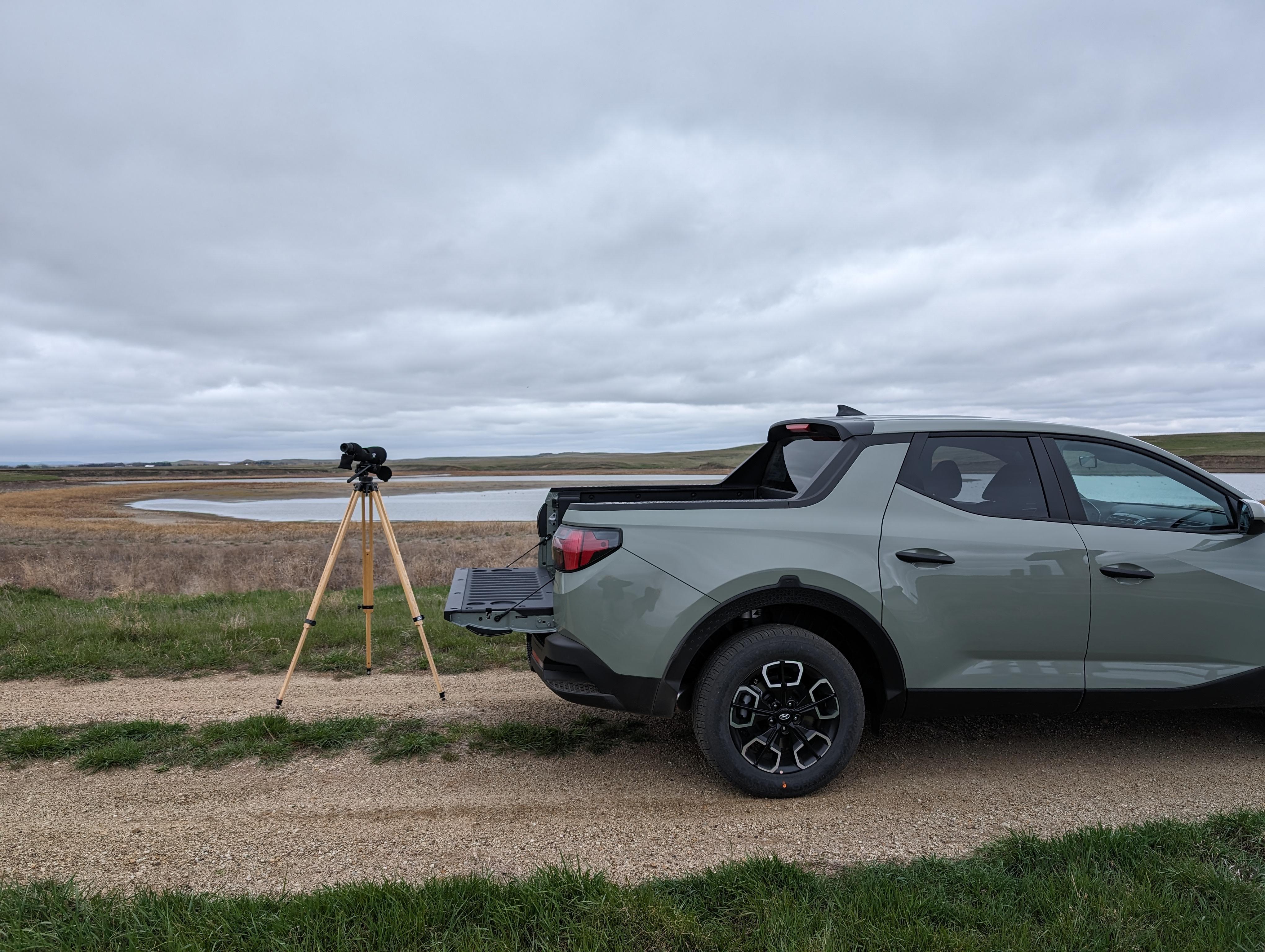 Spotting scope behind a small pickup looking at a water body for birds